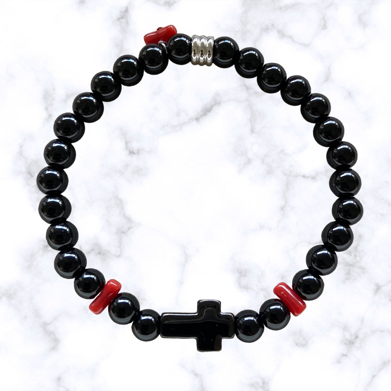 Bracelet élastique en perles d'Onyx noir. Au centre une croix noire en acier inoxydable entourée de petits morceaux de corail rouge de Méditerranée.L'Onyx renforce l'estime de soi et la confiance en soi.Le Corail protège, porte bonheur et éloigne le mauvais œil.